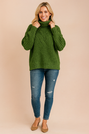 Olive green chunky cable-knit turtleneck sweater with ribbed cuffs and hem, styled with distressed blue skinny jeans and tan suede flats