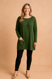 Olive green oversized tunic with drop shoulders, long sleeves, single front patch pocket, and a boat neckline, styled with black leggings and taupe pointed-toe heels.