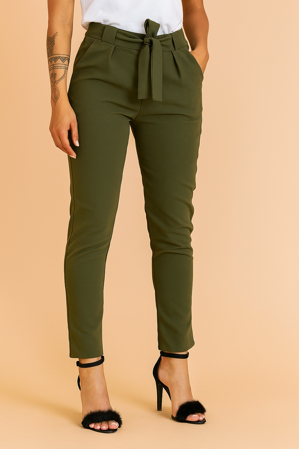 Olive green high-waisted slim-fit trousers with a tie-front belt, pleated detailing, and slanted pockets, styled with black faux fur high-heeled sandals.