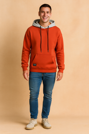 Men’s casual orange hoodie with grey hood lining, featuring black drawstrings and a front kangaroo pocket, styled with slim-fit blue jeans and light beige lace-up shoes.