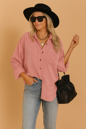 Oversized pink corduroy button-up shirt with chest pocket and rolled sleeves, styled with light wash denim jeans and accessorized with layered gold chains and a black drawstring handbag.
