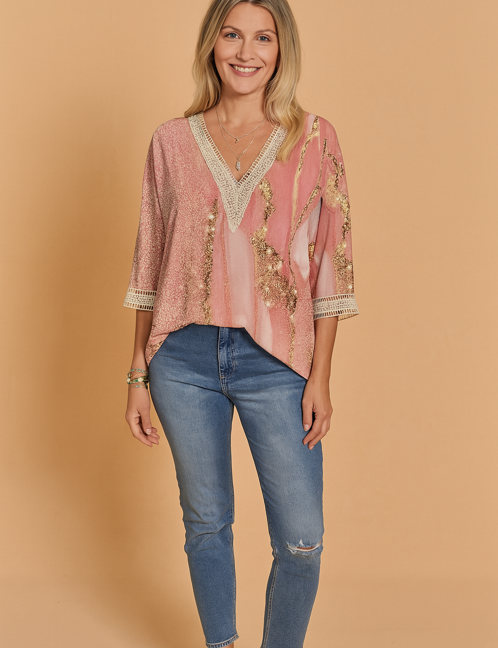 Pink and gold abstract print V-neck blouse with crochet lace trim on the neckline and sleeve cuffs, styled with blue distressed jeans.