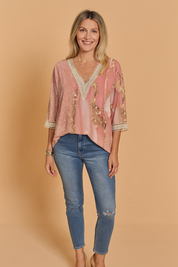 Pink and gold abstract print V-neck blouse with crochet lace trim on the neckline and sleeve cuffs, styled with blue distressed jeans.