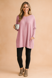 Pastel pink oversized long-sleeve knit sweater with front patch pockets, styled with black leggings and taupe suede ankle boots.