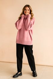Soft pink oversized turtleneck sweater with ribbed hem and cuffs, paired with tailored black trousers and black loafers for a modern pastel-meets-neutral look.
