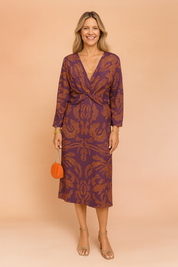 Elegant purple co-ord set featuring a twist-front long-sleeve blouse and matching high-waist midi skirt with intricate burnt-orange paisley pattern.