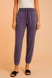 Purple jogger pants with a soft washed finish, featuring an elastic waistband with drawstring, slanted front pockets, and elasticated cuffs for a tapered fit.