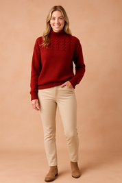 Deep red cable-knit high-neck sweater with ribbed cuffs and hem, paired with beige slim-fit pants and tan ankle boots.