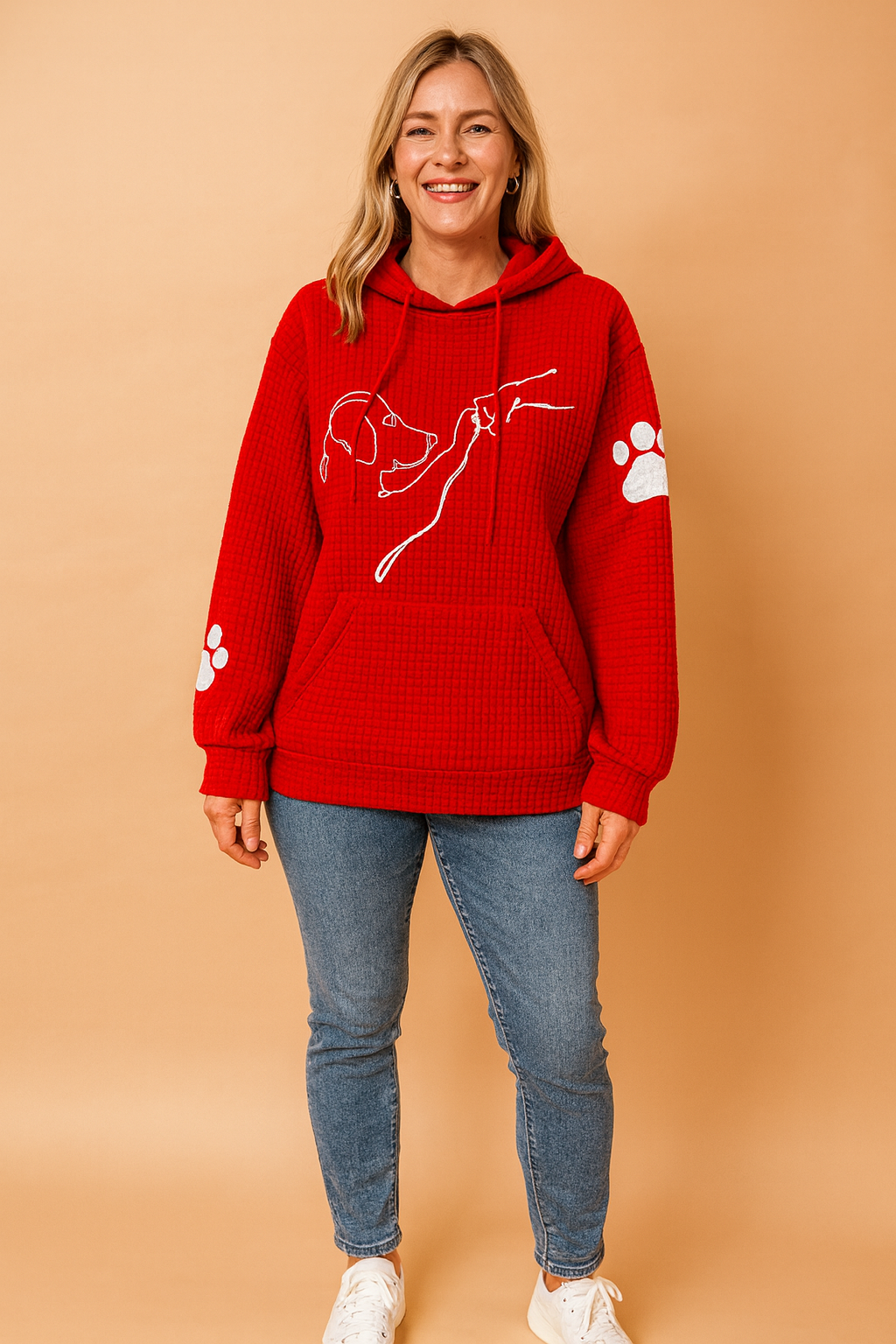 Red waffle-textured hoodie with a white minimalist dog-and-hand line illustration across the chest and white paw print accents on both sleeves, paired with light blue slim-fit jeans and white sneakers.