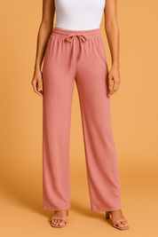 Wide-leg pleated pants in rose pink with a drawstring waistband and vertical rib texture, styled with nude block-heeled sandals and a tucked-in white tank top.