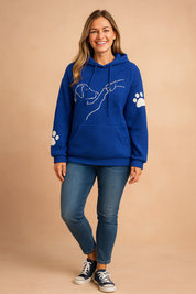 Royal blue waffle-knit hoodie with front kangaroo pocket, white minimal dog line art and paw print details on sleeves, styled with medium-wash skinny jeans and navy canvas sneakers.