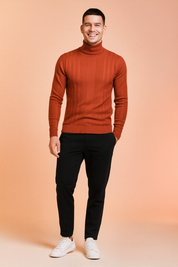 Men’s rust-colored ribbed turtleneck sweater with vertical textured patterns, paired with black slim-fit trousers and white sneakers.