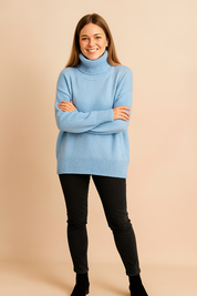 Oversized sky blue knit turtleneck sweater with thick ribbed collar, cuffs, and hem, styled with fitted black jeans and black ankle boots.
