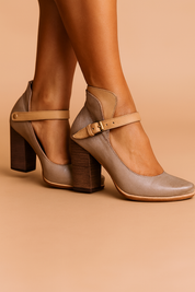 Taupe leather Mary Jane block heel shoes with tan straps, brass buckle, rounded toes, and wood-textured chunky heels, crafted in smooth matte leather finish with detailed stitching and slight natural creasing.