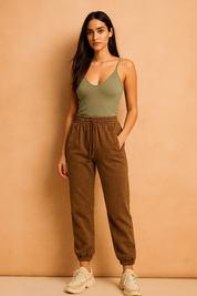 Brown high-waisted jogger pants with elastic cuffs, subtle washed finish, and side welt pockets styled with a drawstring waistband, paired with off-white chunky sneakers.