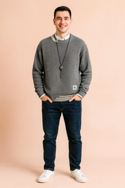 Ribbed crew neck sweater in dark gray with cream contrast collar detail, white inner shirt, stripe accents on cuffs and hem, and a decorative pendant necklace.