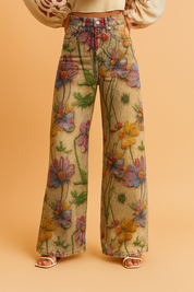 Wide-leg high-waisted jeans with a vibrant all-over floral print in purple, orange, red, and green tones, featuring a five-pocket design and a button fly closure, styled with open-toe sandals.