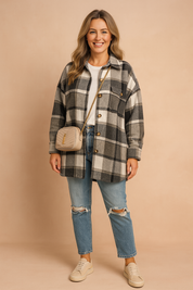 Oversized plaid shacket in black, grey, and white tones with large tortoiseshell buttons, paired with distressed blue denim jeans and a white crew-neck tee, styled with a beige quilted crossbody bag and cream low-top sneakers.