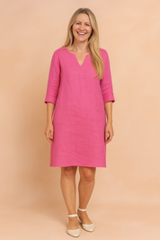Vibrant pink V-neck shift dress with three-quarter sleeves, knee-length hem, and clean minimal silhouette, styled with cream ankle-strap flats for a fresh, everyday look.