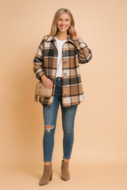 Women's oversized plaid shacket in tan, white, and black tones, styled over a classic white crew-neck tee and paired with ripped skinny blue jeans and taupe ankle boots, complemented by a beige quilted crossbody bag.
