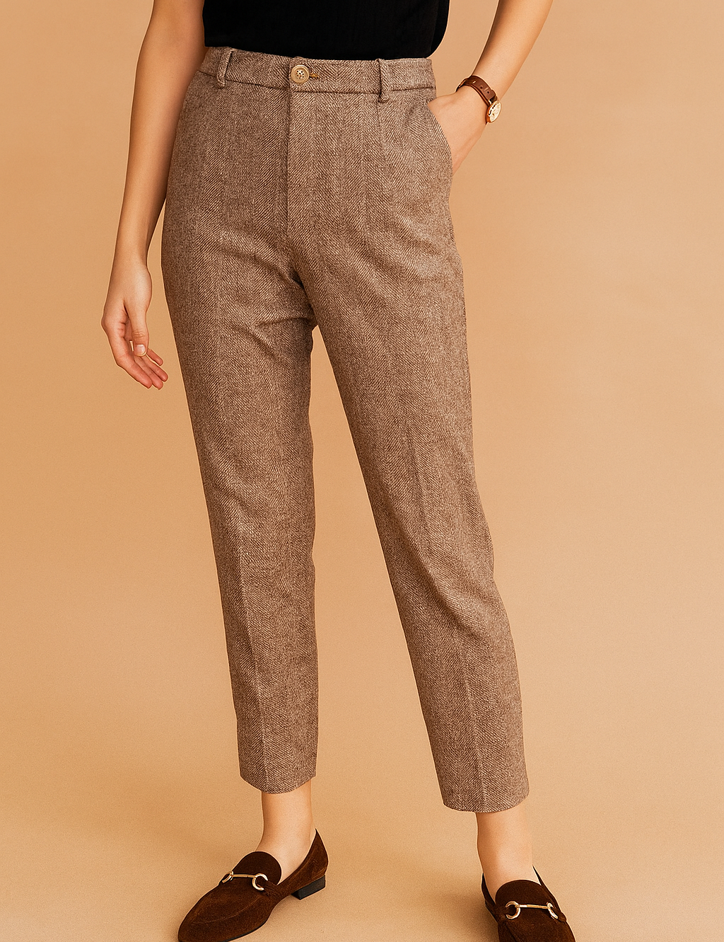 Tailored taupe herringbone trousers with a classic front pleat, high waist, and ankle-length cut, paired with dark brown suede loafers featuring gold hardware.