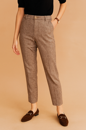 Tailored taupe herringbone trousers with a classic front pleat, high waist, and ankle-length cut, paired with dark brown suede loafers featuring gold hardware.