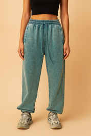 Relaxed-fit teal acid-wash jogger sweatpants featuring an elastic waistband with drawstring, straight leg silhouette, and rolled cuffs, paired with chunky gray athletic sneakers.