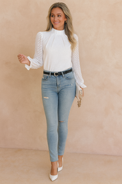 Elegant long-sleeve blouse with pleated front and chevron mesh sleeves, styled with high-waisted ripped jeans, a black belt, and pointed white heels.