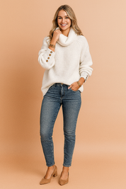 White ribbed cowl neck sweater with bronze button detailing on sleeves, styled with mid-wash skinny jeans and camel suede block heels