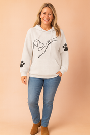 White waffle-textured hoodie with black minimalist dog illustration and paw print graphics on sleeves, styled with mid-rise skinny jeans and navy lace-up sneakers.