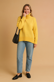 Pastel yellow oversized knit turtleneck sweater with ribbed cuffs and hem, paired with light-wash straight denim jeans and black leather loafers, styled with a minimalist black shoulder bag.