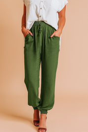 Olive green drawstring jogger pants with front patch pockets and elastic cuffs, styled with a tucked-in white button-up blouse and brown heeled sandals.