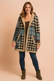 Patchwork fleece-lined hooded coat featuring large beige polka dots, intricate teal and rust ethnic motifs, and cozy tan sherpa trim, styled over a fitted top with skinny jeans and suede ankle boots.