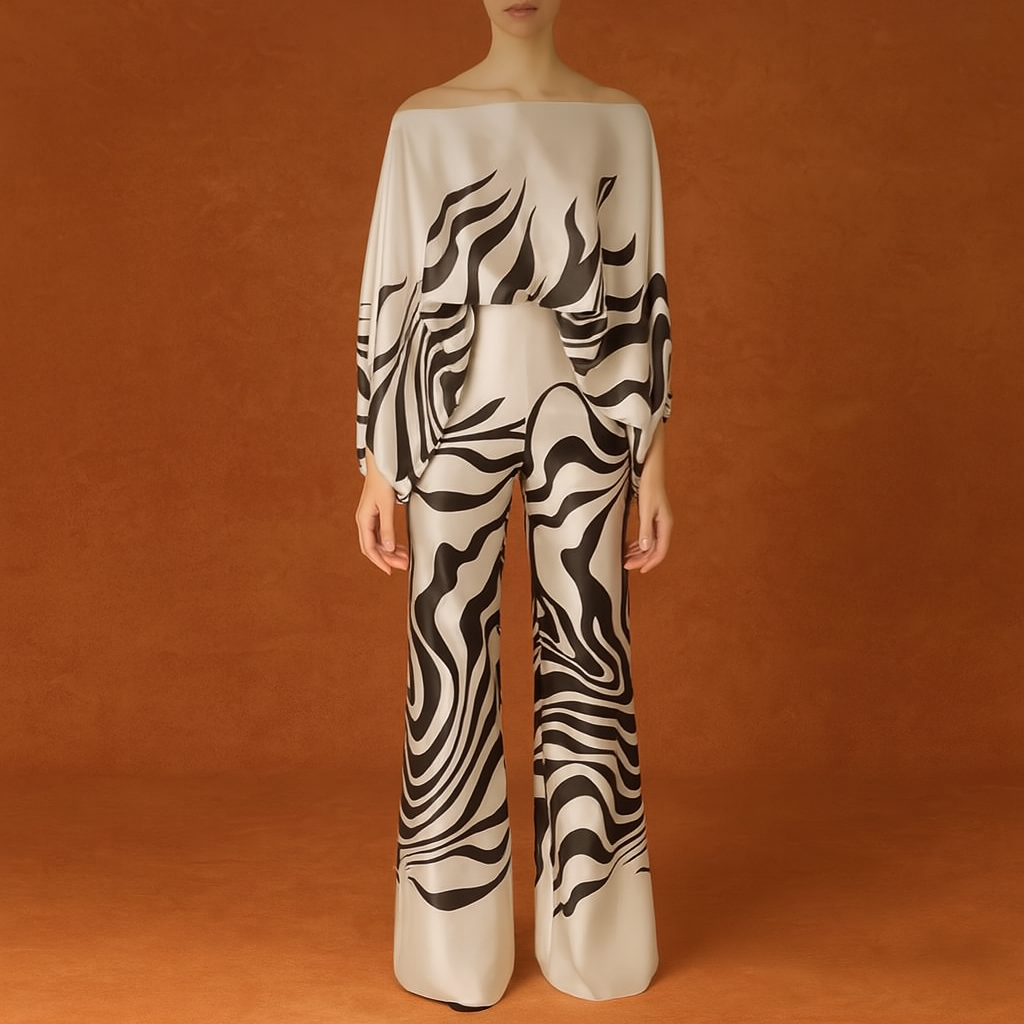 Satin coord set featuring a loose off-shoulder top and wide-leg trousers, both printed with bold black abstract wave patterns on a creamy beige base. The luxurious fabric has a smooth, high-sheen finish that enhances the fluidity of the draped silhouette, creating a refined and artistic statement look.