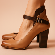 Two-tone tan and dark brown leather block heel pumps with a smooth matte finish, rounded toe, stacked wooden heel, and a slender ankle strap featuring a brass buckle closure.