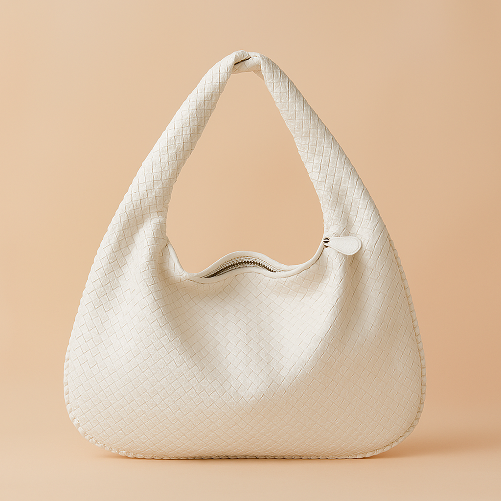 White woven crescent hobo bag with zip closure, displayed against a warm pastel peach-beige backdrop in soft studio lighting.