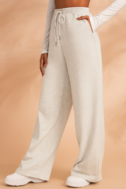 Wide-leg light heather gray sweatpants with an elasticated waistband and drawstring, styled with subtle front seams and paired with white platform sneakers for a casual yet polished athleisure look.