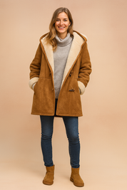 Camel brown faux suede shearling coat with toggle closure, cream sherpa lining, rolled cuffs, and structured seams, layered over a light gray turtleneck sweater and styled with dark denim jeans and tan suede winter boots.