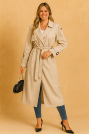 Beige belted trench coat with storm flaps and button details, styled with slim blue jeans, black heels, and a black handbag with chain strap.