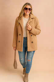 Camel teddy coat with double-breasted buttons, styled with a cream sweater, distressed blue jeans, taupe ankle boots, and a beige handbag.