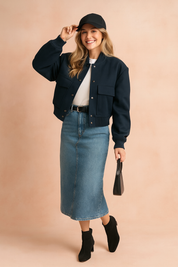 Cropped navy bomber jacket with snap buttons and front pockets, paired with a white T-shirt, high-waist denim midi skirt, black ankle boots, and a black