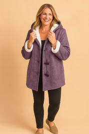 Purple suede duffle coat with white faux shearling lining and cuffs, toggle button closure, paired with black slim-fit pants and taupe loafers.