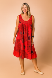 Sleeveless red sundress featuring bold black mandala-style circular prints, gathered scoop neckline, and an airy A-line silhouette designed for a relaxed, breezy fit.