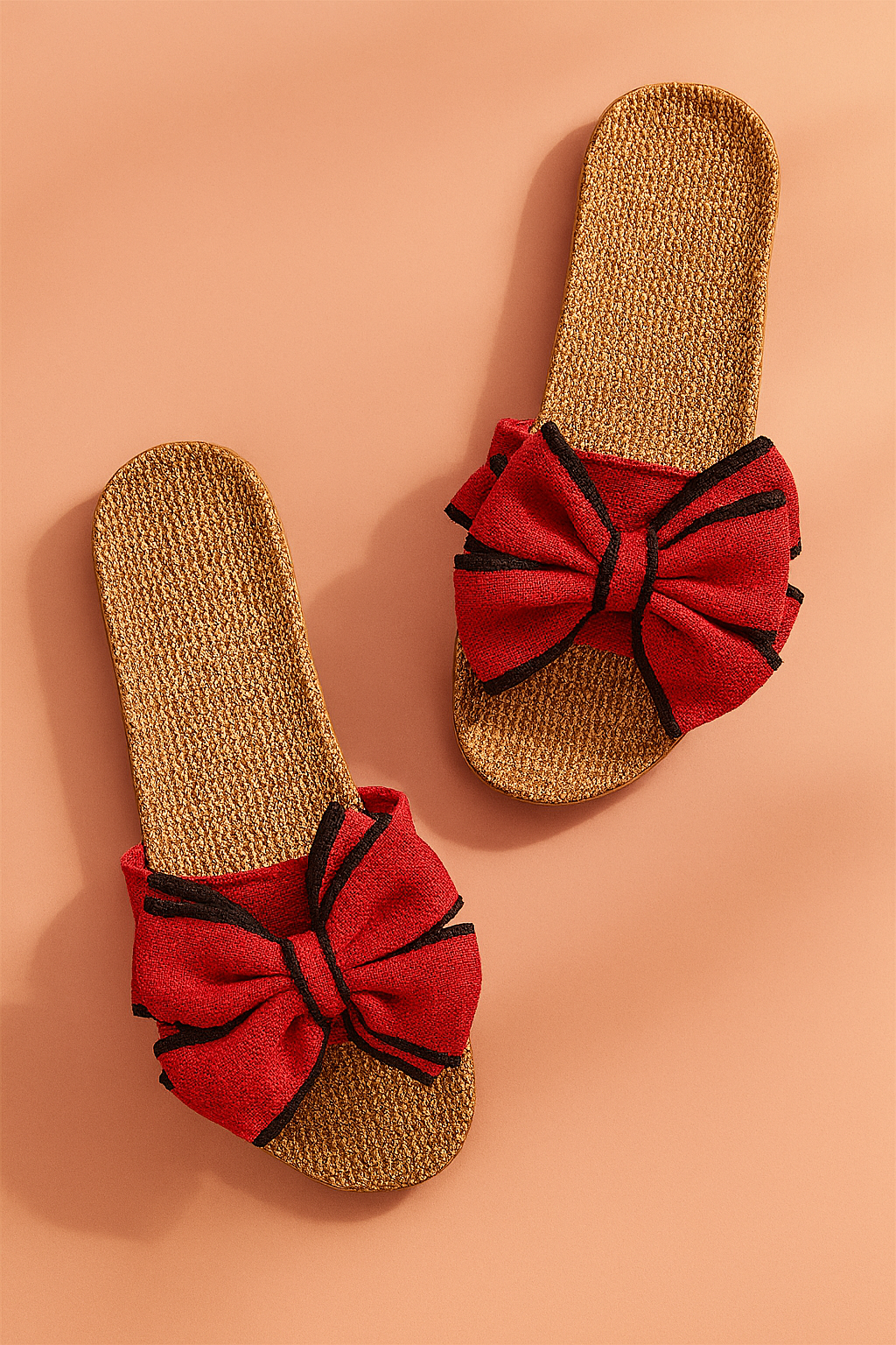 Red bow slide sandals with woven jute soles and black-trim accents on the bows, designed for a casual yet bold summer look.