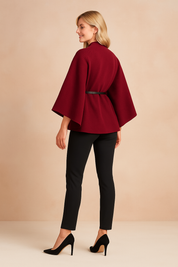 Elegant women's red cape-style jacket with side belt detail, long sleeves, and tailored fit, shown from the side for design emphasis.