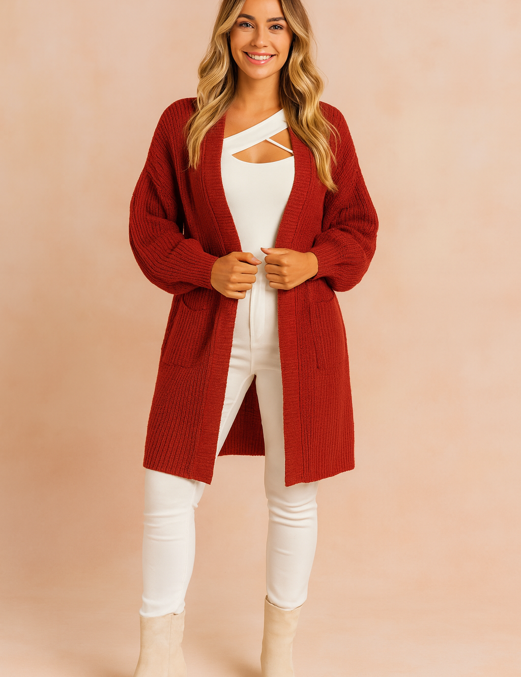 Deep red oversized chunky knit cardigan with open front, long sleeves, and two front patch pockets, styled over a white top and white fitted pants with beige suede ankle boots.