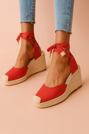 Vibrant red espadrille wedge sandals with closed canvas toes, natural jute-wrapped platform soles, and red ankle-wrap fabric ties with metallic grommet accents.