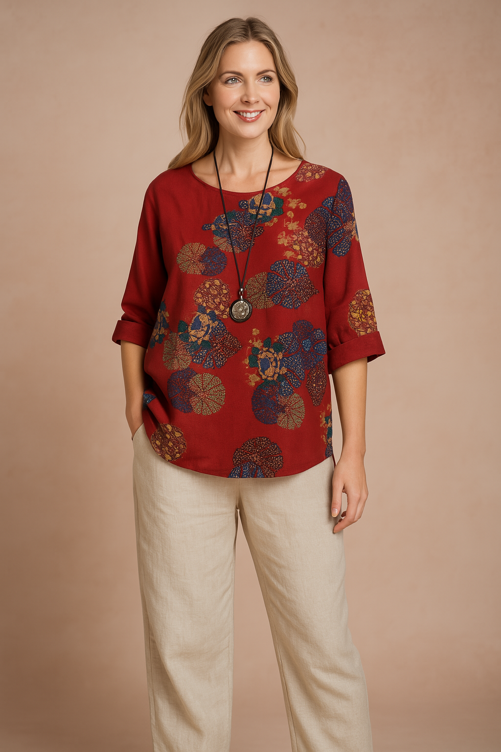 Boho-inspired red blouse with vibrant multicolor circular floral patterns, diagonal button accents at the neckline, and mid-length sleeves, styled over loose beige trousers for a casual artistic look.