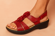 Red leather open-toe sandals with layered floral appliqués, featuring a cushioned beige insole, black wedge outsole, and secure Velcro ankle strap.