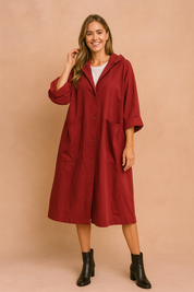 Oversized red hooded coat with button-down front, wide sleeves, and large front patch pockets, styled with black ankle boots.